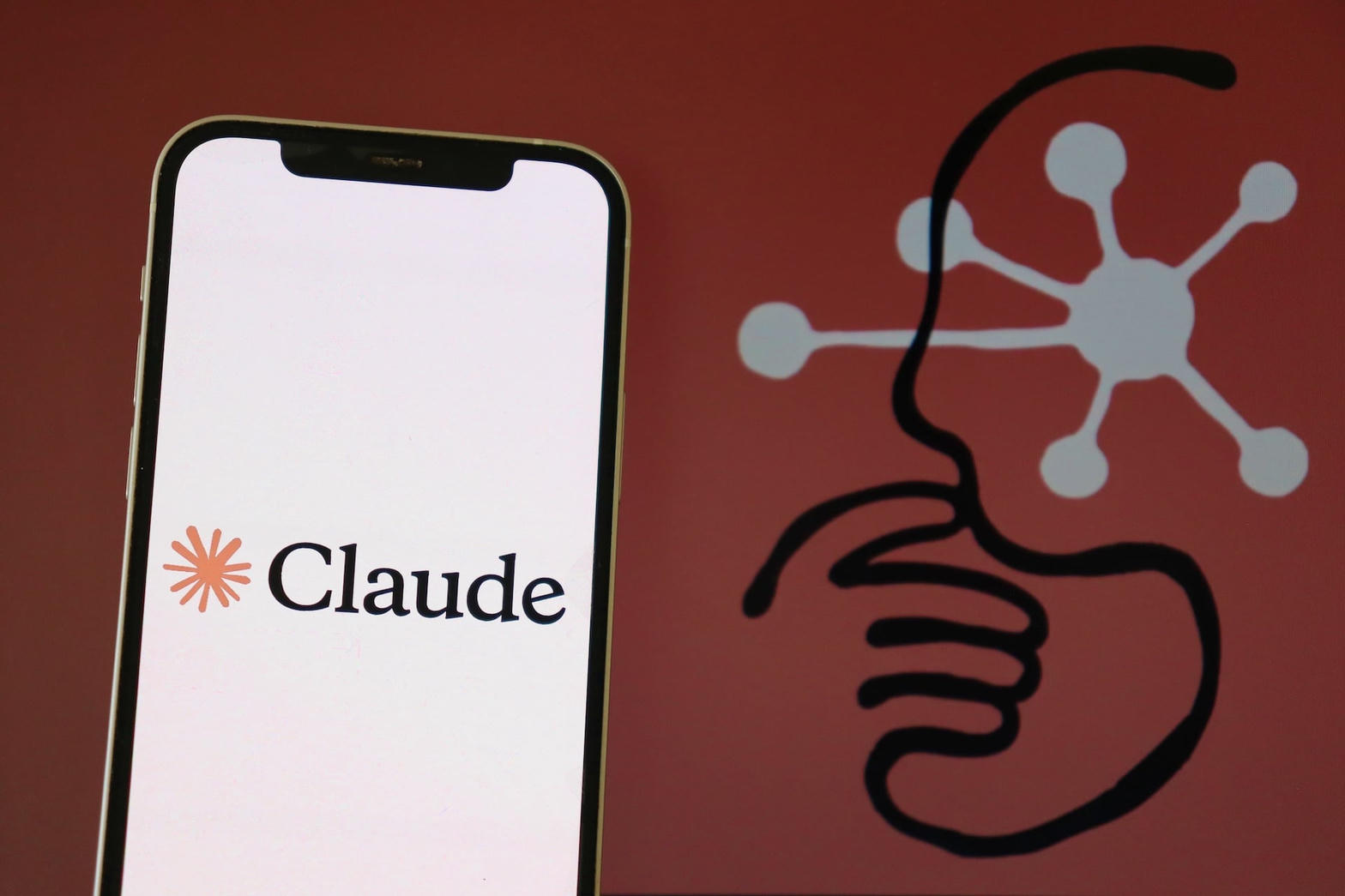 Claude wordmark on a phone in front of the Anthropic asterisk logo